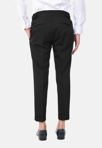 Pantaloni neri su misura con una vestibilità slim, fronti plissé e due tasche posteriori. L'orlo è arrotolato, abbinato a scarpe scure e una camicia bianca.