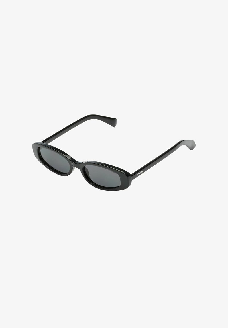 Lunettes de soleil ovales noires avec verres solides foncés et branches droites, inclinées légèrement vers le haut sur fond blanc.