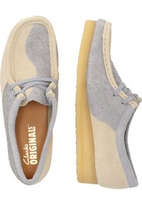 Chaussures en daim gris clair et crème avec un détail en lacets, bout rond et une semelle en caoutchouc beige épaisse. Caractérisées par une texture douce et un design décontracté.