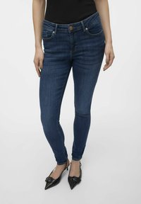 Jeans skinny azul oscuro de mezclilla, con cierre de botón, dos bolsillos frontales y una textura suave. Acentuados con detalles de costura.