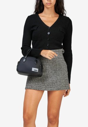 Zwarte geribde cardigan met V-hals, gecombineerd met een gestreepte minirok en een kleine zwarte handtas met een zilveren accent.