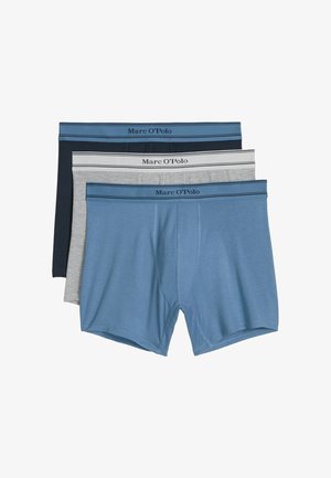 Trois boxers pliés pour hommes en bleu, gris et noir avec des ceintures Marc O’Polo marquées, empilés sur un fond blanc.