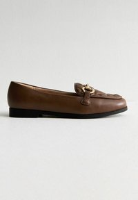 Brauner Lederloafer mit runder Zehenform, dekorativem Schnallen-Detail und flacher schwarzer Sohle. Glatte Textur und minimalistisches Design.