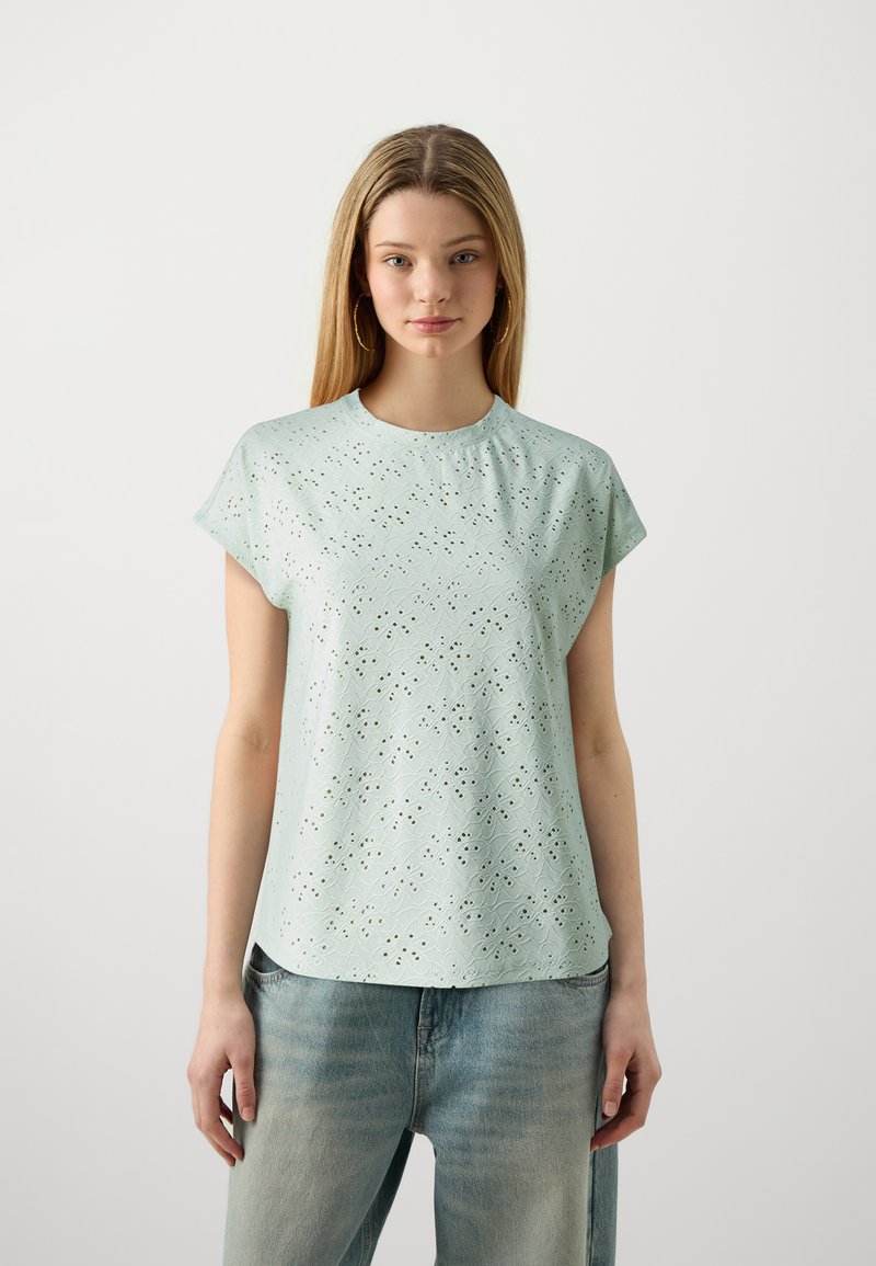 Top corto de manga corta verde claro con un patrón texturizado que presenta cortes, cuello redondo y un ajuste holgado. Combinado con jeans azules desgastados.