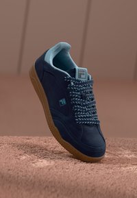 Navy suede sneaker with light blue accents and woven laces, featuring a rubber outsole and a logo on the side and tongue.