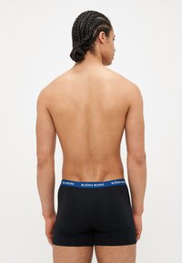 Boxers noirs avec une ceinture bleue "BJÖRN BORG". Design simple, coupe ajustée, texture de tissu lisse. Modèle de dos face à la caméra.