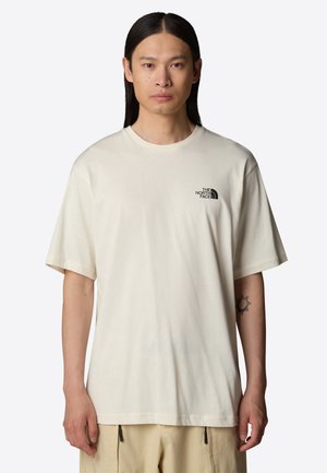 Beige Baumwoll-T-Shirt mit kurzen Ärmeln, Rundhalsausschnitt und einem schwarzen Logo auf der linken Brust. Weicher Stoff, lässige Passform.