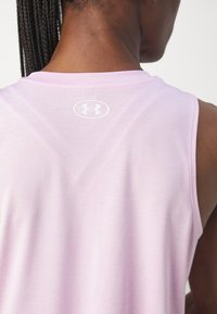 Ljusrosa ärmlös atletisk topp, tillverkad av mjuk tyg, har en subtil logotyp på baksidan och en ren, minimalistisk design.