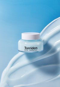 Torriden DIVE IN Rauhoittava Kermassa kirkkaassa purkissa valkoisella kannella. Kerman väri on vaaleansininen, koostumus on silkkinen, taustalla virtaava kermakuva.