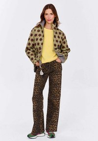 Zelená tlačená bunda s hnedými bodkami, žltý sveter, hnedé zvieracie vzorované nohavice a multicolor tenisky. Neformálny outfit.