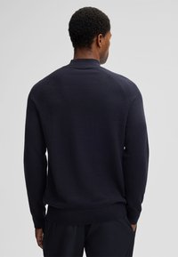 Navy gestrickter Pullover mit hohem Kragen, Raglanärmeln und Rippbündchen. Die Textur wirkt weich und gleichmäßig, geeignet für Freizeitbekleidung.