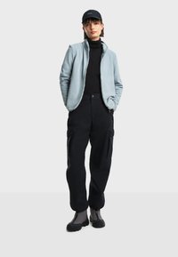 Svijetloplava flis jakna, crni rolak, crne cargo hlače i sive čizme. Jakna ima cijeli zip i opušteni kroj.