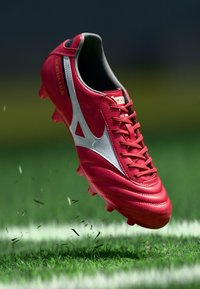 Crampon de fotbal roșu cu accente argintii, superior din piele texturată și șase cuie pentru tracțiune. Designul include un logo și un sistem de șnururi.