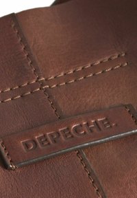 Bruine leren portemonnee met het gegraveerde "DEPECHE" logo. Kenmerkt zichtbare stiksels en een gladde textuur, wat een rechthoekig ontwerp benadrukt.
