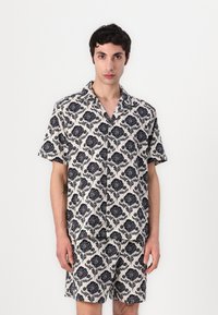 Σετ κοντομάνικης μπλούζας και σορτς σε κρέμ απόχρωση με ναυτική λουλουδάτη σχέδιο, διαθέτει χαλαρή εφαρμογή και γιακά, κατασκευασμένο από ελαφρύ ύφασμα.