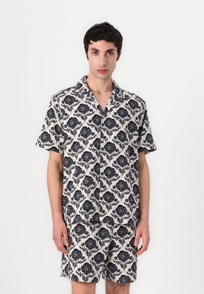 Σετ κοντομάνικης μπλούζας και σορτς σε κρέμ απόχρωση με ναυτική λουλουδάτη σχέδιο, διαθέτει χαλαρή εφαρμογή και γιακά, κατασκευασμένο από ελαφρύ ύφασμα.