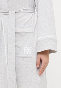Accappatoio di cotone grigio con cintura, tasca a toppa e piping a contrasto. Il logo DKNY è stampato in bianco sulla tasca.