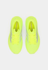 Νεον κίτρινα παπούτσια τρεξίματος με επάνω μέρος από διαπνέον δίχτυ, αντανακλαστικές ασημί ρίγες και επίπεδους κορδόνια. Διαθέτουν διάτρητη περιοχή στα δάχτυλα για αερισμό.