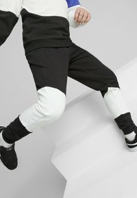Schwarz-weiße Sporthosen mit strukturiertem Finish und Farbblockdesign; kombiniert mit schwarzen Turnschuhen. Die Hosen verfügen über elastische Bündchen.