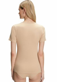 T-shirt aderente beige con maniche corte, scollatura rotonda, texture morbida e tessuto liscio, mostrata da dietro su uno sfondo neutro.