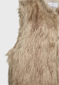 Beige vest i imiteret pels uden ærmer med blød tekstur og en synlig hvid tøjetiket nær halsudskæringen på en hvid baggrund.