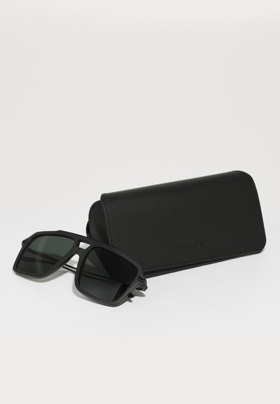 Ochelari de soare negri cu un design pătratic și lentile întunecate, însoțiți de o carcasă elegantă din piele neagră. Rama are o textură mată.