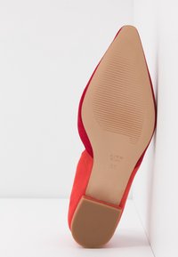 Chaussure plate en daim rouge avec bout pointu, semelle texturée couleur cuir clair et petit talon marron, taille 36, positionnée semelle vers le haut sur fond blanc.
