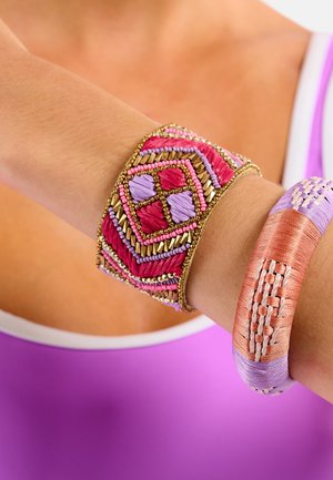 Bracelet à perles aux tons rose, violet et or avec des motifs géométriques ; associé à un bracelet large tissé lisse aux teintes pastel.