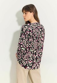 Langärmlige Bluse mit floralem Muster in Schwarz, Pink und Creme. Leichtes Material mit lockerer Passform und abgerundetem Saum.