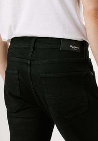 Mustad denim püksid, mis on slim fit lõikega, struktuursete tagataskutega ja nahast brändiplaadikesele vööl. Tekstuuriga kangas.