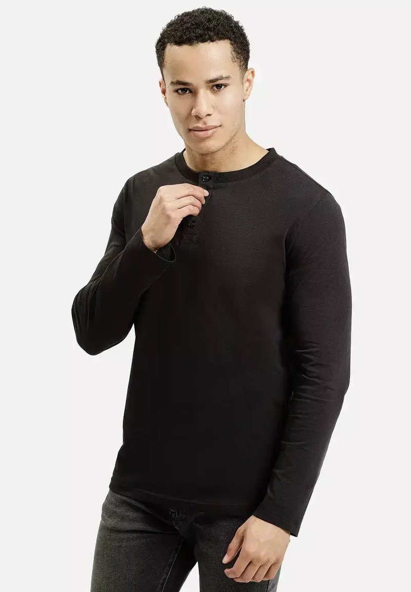 Czarna, długozasłonowa koszula henley z bawełny, z okrągłym dekoltem i plakatą na trzy guziki, noszona na szarych dżinsach. Gładka faktura.