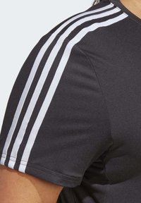 Svart idrettsgenser med korte ermer, glatt stoff og tre hvite striper langs skulderen. Minimalistisk design med rund hals.