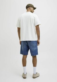 T-shirt bianca a maniche corte, pantaloni shorts in denim, scarpe grigie chiare, calzini bianchi e un cappellino marrone. Design semplice con una vestibilità comoda.
