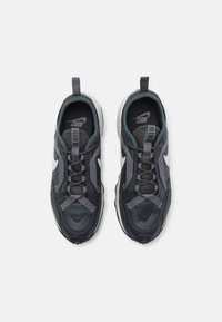 Yhdistelmä mustia ja harmaita Nike-tennareita, joissa on valkoiset swooshit, verkko- ja nahkapinnat sekä silmukkapullot, katsottuna ylhäältä valkoista taustaa vasten.