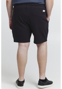 Svarte bomullsshorts med elastisk midje, baklomme og glatt tekstur, som ender rett over knærne.