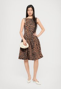 Haljina s leopardskim uzorkom u smešnim i crnim tonovima, s uskim gornjim delom i raširenom suknjom, uparena s kremastom torbicom i svijetlim potpeticama.