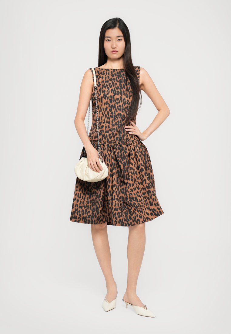Robe à imprimé léopard marron et noir avec un corsage ajusté et une jupe évasée, associée à un sac à main crème et des mules à talons de couleur claire.