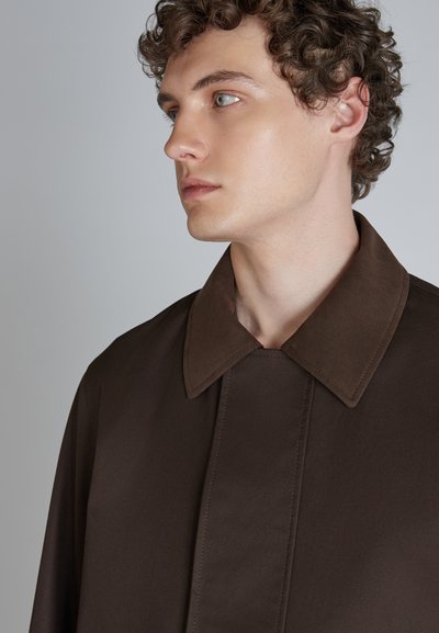 Camisa marrón con cuello hecha de una tela suave; presenta un gran cuello, costura central y líneas limpias para un aspecto estilizado.
