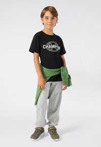 Svarte grafiske t-skjorter med "CHAMPION"-logo, grå joggebukser, grønn hettegenser bundet rundt livet, og grønne joggesko med hvite såler.