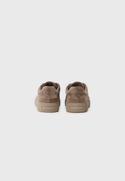 Pair of brown suede sneakers with beige rubber soles, viewed from the back, featuring "Tiger of Sweden" branding on the heel.