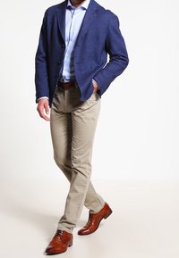 Námořnický vlněný blazer, světle modrá košile, béžové chinos kalhoty a hnědé kožené společenské boty. Blazer má klopový límec a zapínání na jeden knoflík.