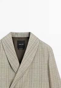 Beige geruite blazer met een gekapte kraag, voorzien van fijne verticale en horizontale lijnen in een gestructureerde stof. Binnenlabel zichtbaar.