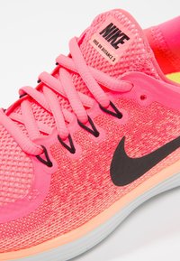 Baskets Nike Free RN Distance 2 en corail lumineux avec un logo swoosh noir, des lacets roses et une tige en mesh texturé.