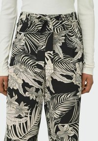 High-waisted trousers in black fabric featuring a large white floral and leaf print, with a belted waist and wide leg design.
