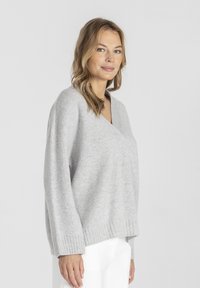 Jasnoszary, dzianinowy sweter z dekoltem w kształcie litery V, długimi rękawami i ściągaczami. Tekstura wydaje się miękka i komfortowa.