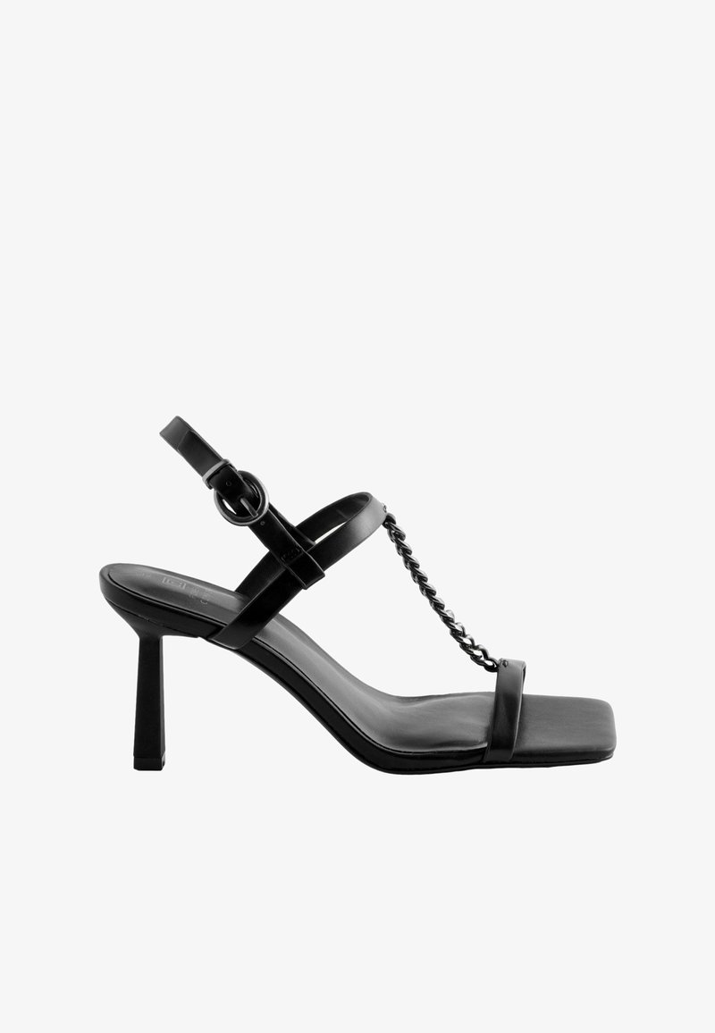 Svarta högklackade sandals med fyrkantig tådesign, tunna remmar, kedjedekor och justerbar ankelsnodd. Tillverkade av glänsande material.