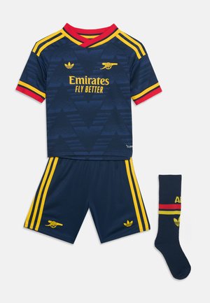 Σκούρο μπλε εμφάνιση ποδοσφαίρου της Arsenal με κίτρινη και κόκκινη λεπτομέρεια, που περιλαμβάνει φανέλα, σορτς και μία κάλτσα με λογότυπα ομάδας και όνομα χορηγού.