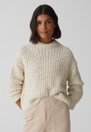 Chunky cream knitted sweater with a ribbed texture and high neckline, paired with light beige ribbed corduroy pants.