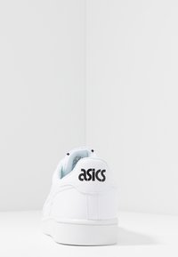 Bílá kožená teniska s texturovaným povrchem, vybavená polstrovaným límcem a černým logem "asics" na patě. Minimalistický design, nízký střih.