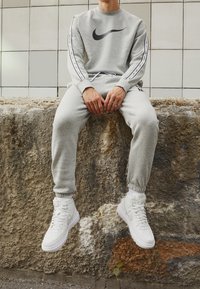Grå Nike sweatshirt med svart logotyp, matchande grå joggers och vita hög-top sneakers. Har elastiska muddar och synlig varumärkesdetaljering.